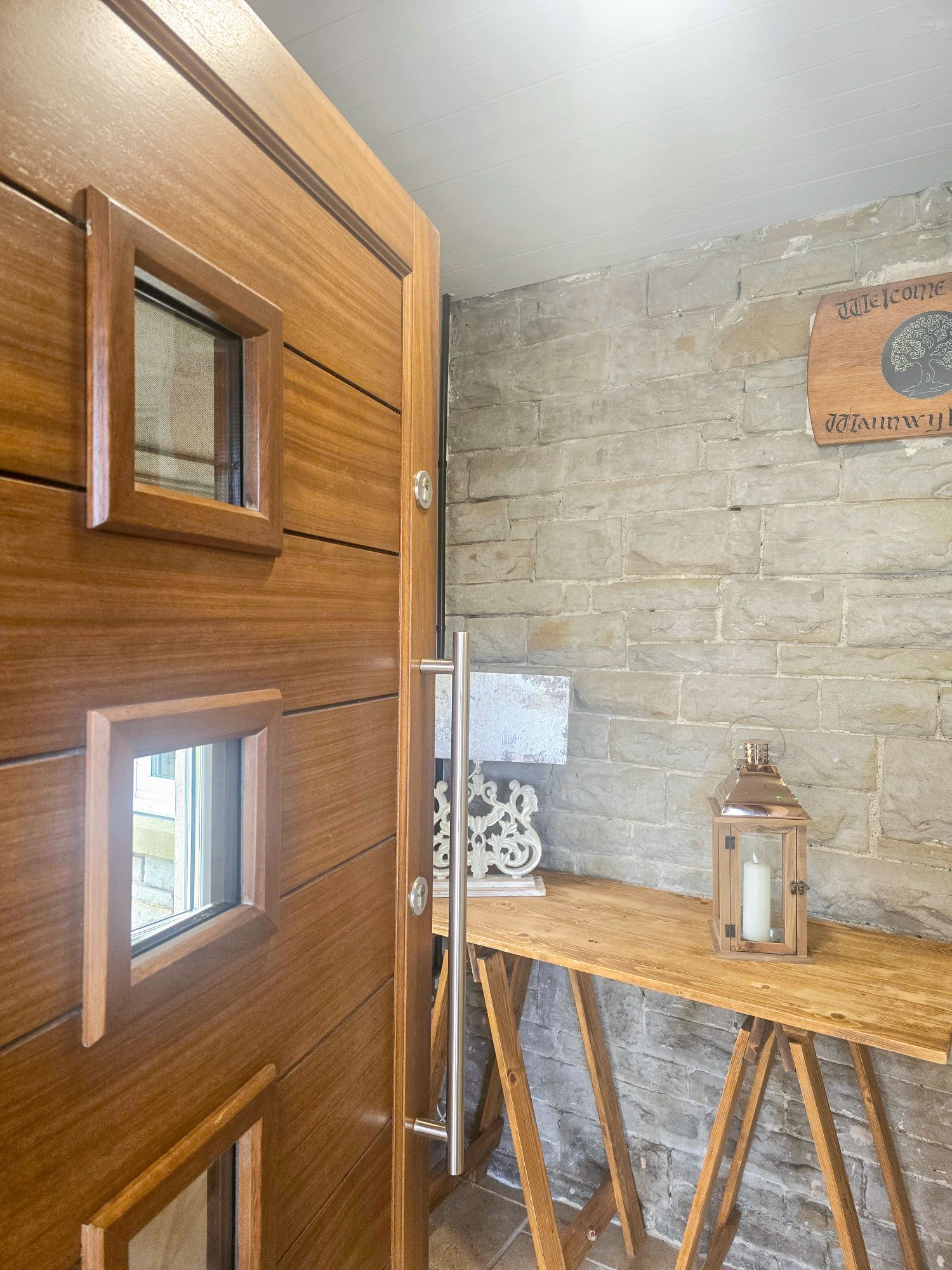 Interior porch view with wooden door, stone wall, welcome sign, and decorative table
