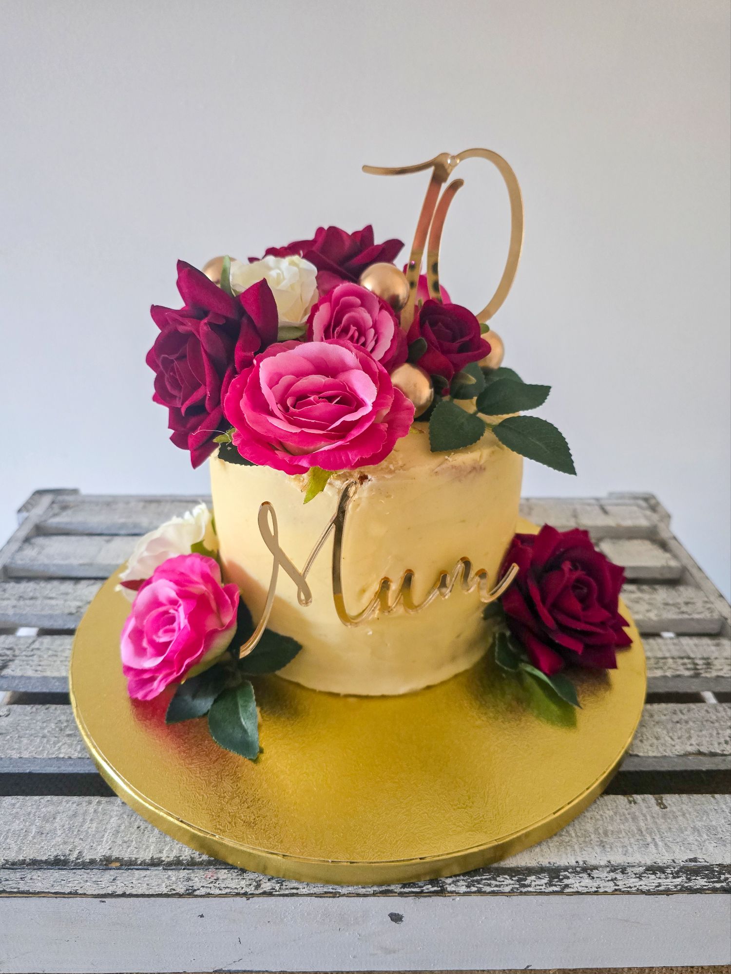 Clotted cream birthday cake with gold topper, florals, and “Mum” sign on wooden crate