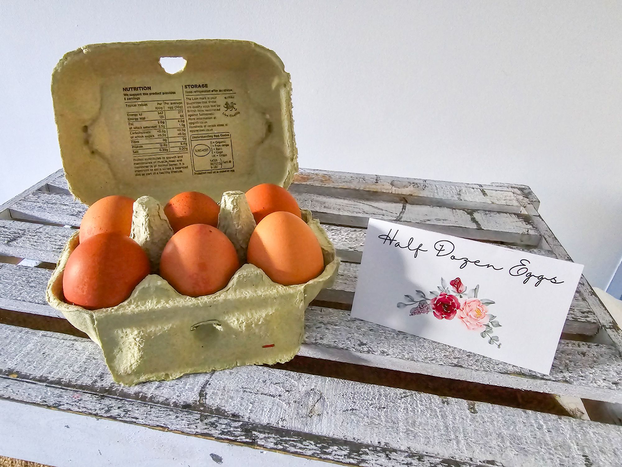 Half dozen eggs with floral “eggs” label on white wooden crate