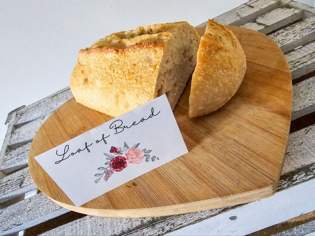 Crusty loaf of bread with floral “bread” label on heart-shaped board
