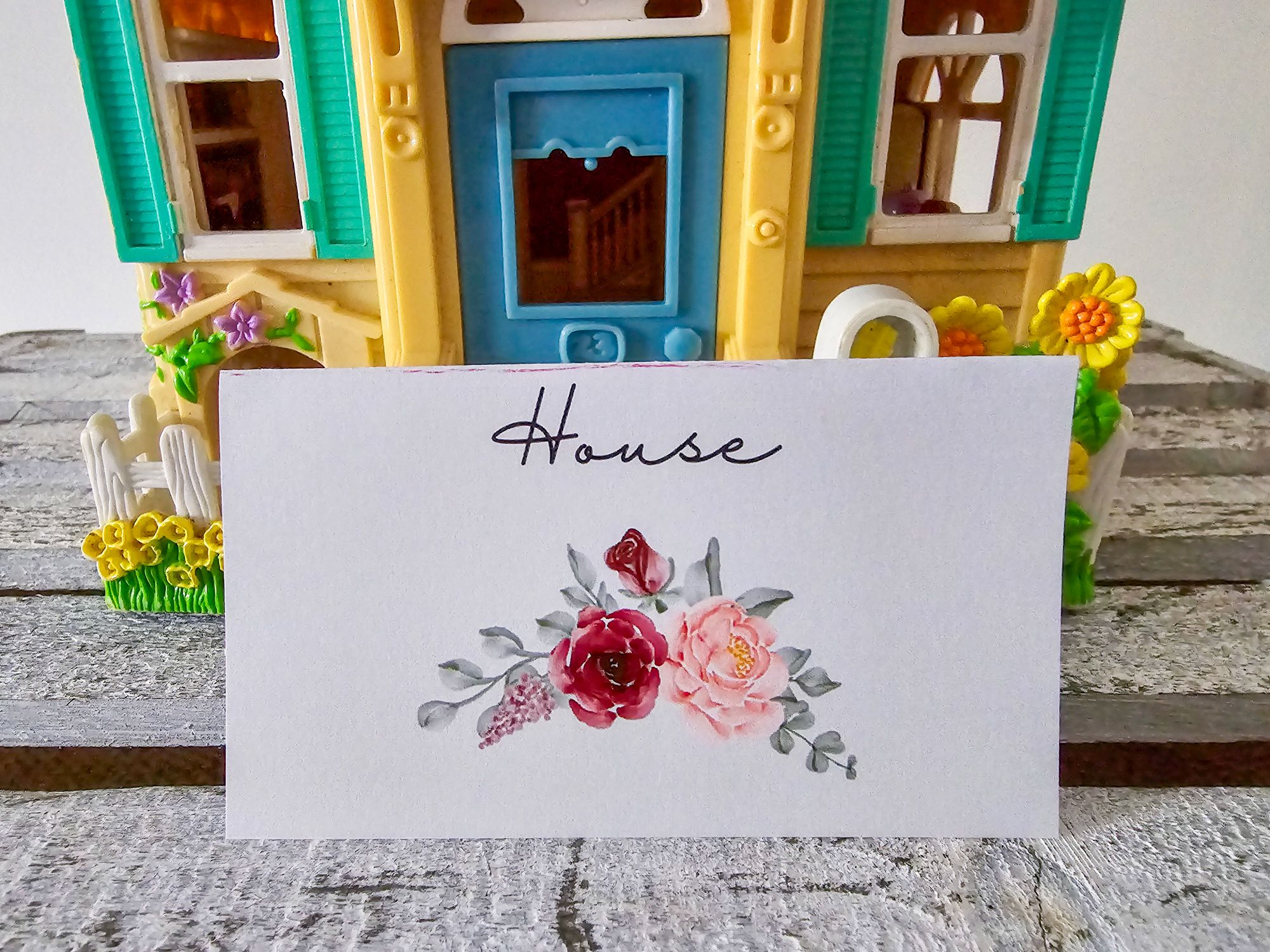 Floral “house” label with yellow toy house and blue door in background