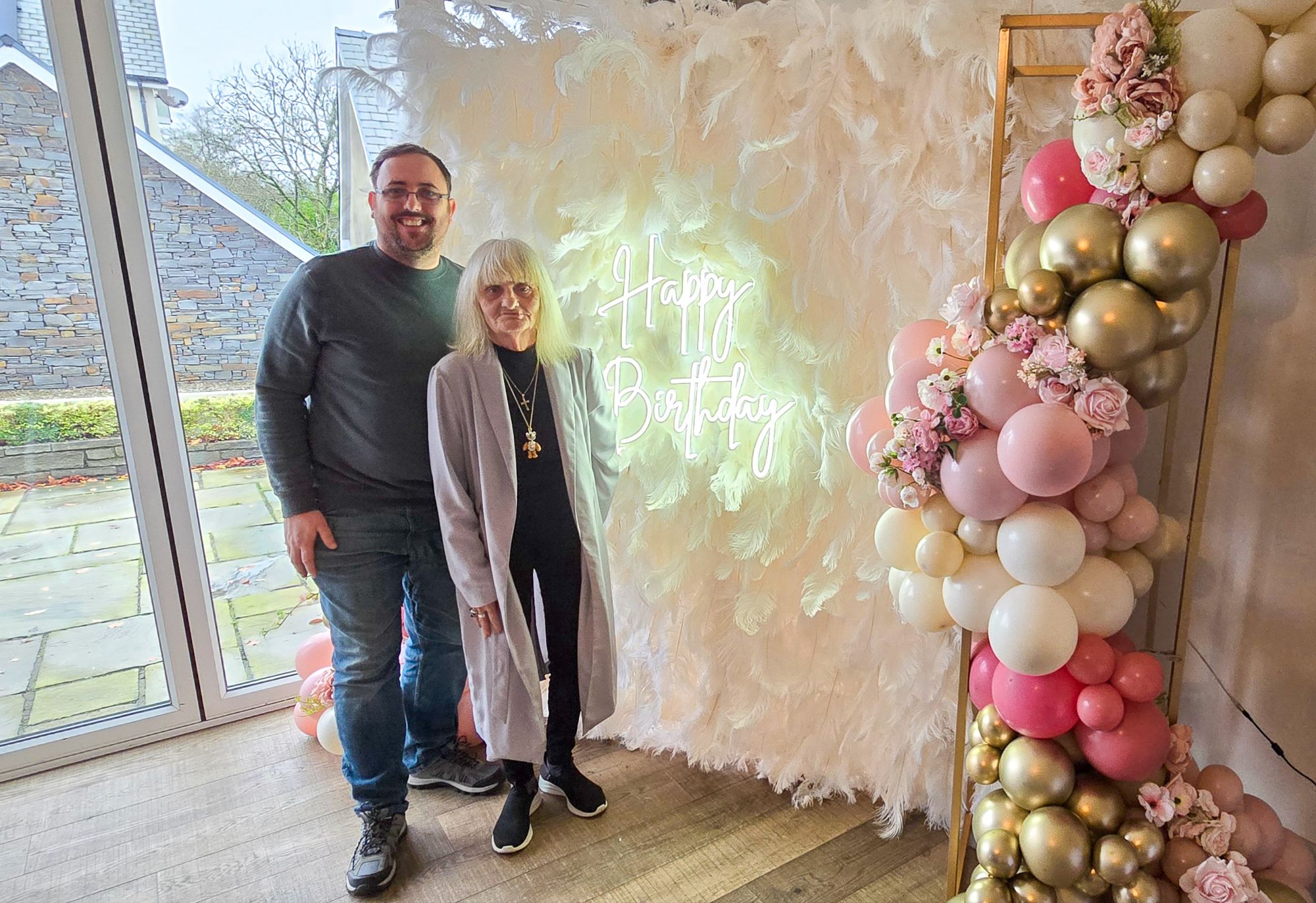 Mum and son in front of feather wall with floral balloon garland