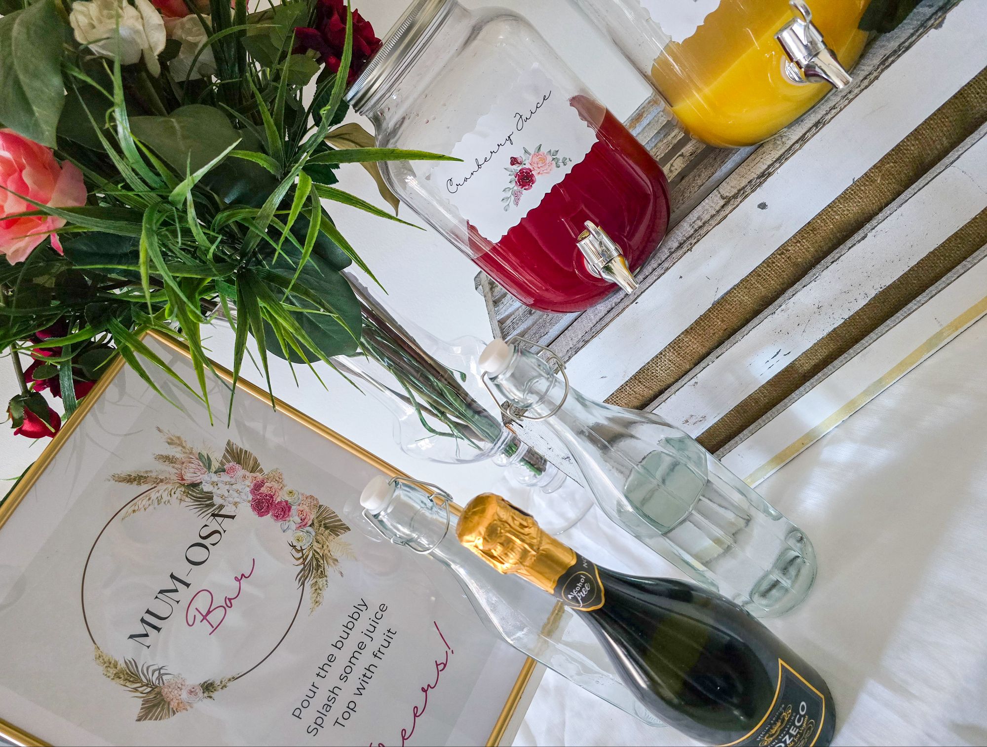 Mum-osa bar setup with floral poster, juice decanters, and prosecco