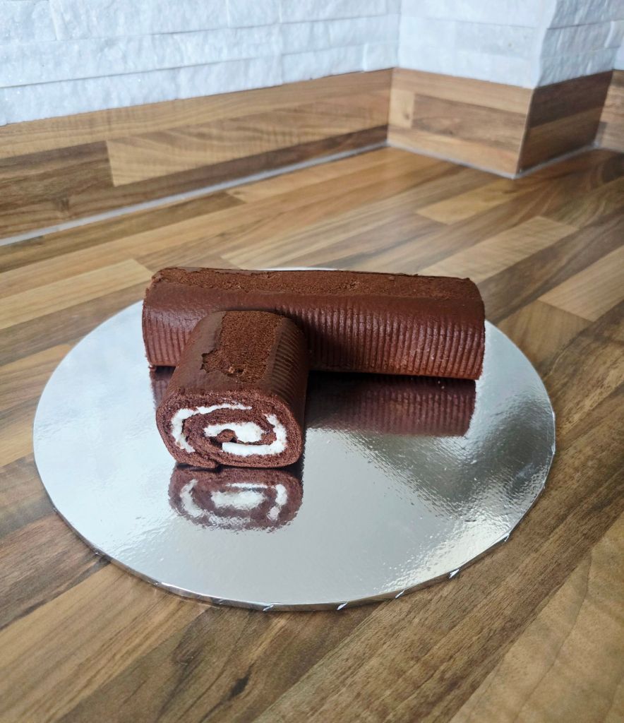 Chocolate Swiss roll on a silver cake board with one end cut and placed to resemble a branch coming out of a trunk, showing the white cream swirl inside.